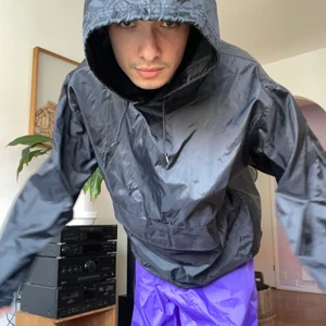 Vintage Nylonhoodie Svart  - En svincool vintagehoodie i nylon som reflekterar solljus unikt i rörelse. ✨🖤 En stor magficka finns med velcro-lås. Remmar finns för att dra åt både luva och midja. Storlek Medium. Modellen är 178cm. 