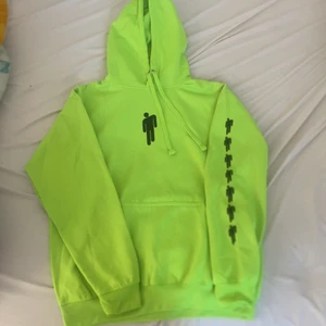 Neon Grön Billie Eilish hoodie - Hoodien är använd max 2 gånger, storlek M. Köpt för 500kr. Säljer för att den inte används längre och för att den har blivit för liten. Den är lite over size, så skulle rekommenderas för folk med storleken S-M. Den ska tvättas i 30 grader (tvätt maskin) Hoodien har loggan (hängande gubbe) längst upp på tröjan och sedan 7st lite mindre på vänster arm.