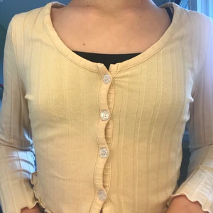 En gul lång ärmad tröja med knappar - Det är en gul tröja med vågigt vid slutet av tröja och vid armarna, det är knappar i mitten av tröjan som man kan knäppa upp om man vill. Tröjan är bara använd en gång men kommer vara tvättad när man får hem den.