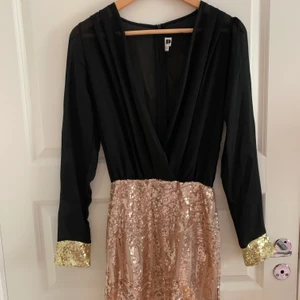 Utsmyckad festkänning från Dennis Maglic - Klänning i lätt genomskinligt tyg med djup urringning och en kort kjol utsmyckad med paljetter. Omlottdesign. Dragkedja baktill. Från Dennis Maglic storlek S (liten i storleken). Aldrig använd. 