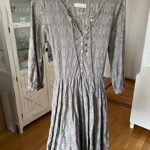 En otroligt vacker klänning, gråbrun med lila band. Kjolen är i lager och har ett fantastiskt fall. Den är i väldigt gott skick. 