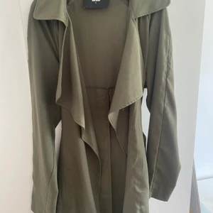 Olivgrön trenchcoat  - Olivgrön trenchcoat i en kort modell från bikbok. Skicket är som helt ny.