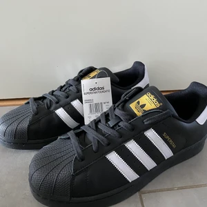 Adidas Superstar Skor - Adidas Superstar Foundation Skor. Svarta med vita träck och guldiga detaljer. Helt nya och obrukade. Klassiska adidas skor, jättesnygga! Kartong medföljer vid intresse.