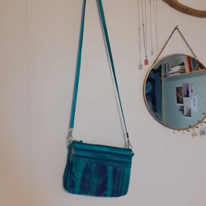 Blå handväska  - Fin blå handväska i tyg. Den har tre rymliga fack och ett justerbart band. Bandet går att ta loss samt flytta runt så att man själv kan välja hur man vill bära väskan. Passar perfekt för fester när man inte vill släpa runt på nycklar och mobil i händerna🌸