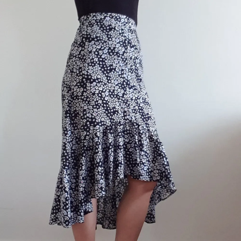En blommig kjol med assymetrisk kant i volang. Från H&M, dragkedja i sidan. Färgen är en mörkare marinblå, nästan svart.. Kjolar.