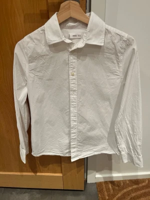 Vit skjorta från MNG, 164 cm/13-14y - Klassisk vit skjorta från MNG i storlek 164 cm. Skjortan har lång ärm, knappar framtill och en stilren krage. Perfekt till många olika outfits och enkel att matcha. Jättefint begagnat skick, knappt använd! Tillverkad i bomull för en skön känsla. Superfin till skolavslutningen eller konfirmationen!🥳💙
