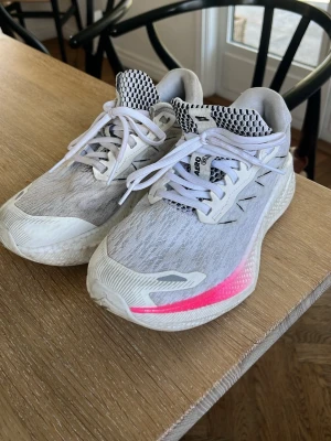Salomon Aero Glide vita sneakers - Lätta och sportiga sneakers från Salomon i modellen Aero Glide. Skorna är vita med grå detaljer och har en tydlig rosa accent på sulan. Ovandelen är i mesh för bra andningsförmåga och sulan är tjock och dämpande. Perfekta för dig som gillar en modern och sportig look. Säljer dessa oroliga skor pågrund av att de är för små. Dom e inte andvända mycket men lite smutsiga därav de låga priset. Köpta för 1800 kr Pris kan diskuteras 