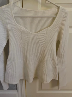 Vit ribbstickad tröja med v-ringning - Säljer en vit ribbstickad tröja med snygg v-ringning och lång ärm. Tröjan har ett diskret mönster framtill och är gjord i ett mjukt, stretchigt material. Perfekt för dig som gillar stilrena och enkla plagg.
