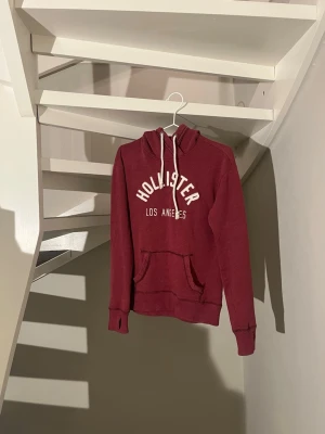 Vinröd hoodie från Hollister XS - Skit fett vinröd hoodie från Hollister med vit text på bröstet. Perfekt för en avslappnad och trendig stil. Pris kan diskuteras vid snabbäffar! Obs har ett litet hål vid fickan men inget man tänker på