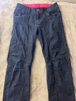 Mörkblå jeans med rosa detaljer PULZ jeans  - Snygga mörkblå jeans från pulz jeans med rosa sömmar och knapp. Baksidan har unika bakfickor med stickat mönster och rosa kant. Insidan av linningen är rosa för en extra pop av färg. Perfekta för dig som vill sticka ut lite extra!