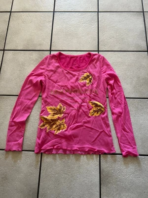 Rosa långärmad topp med bladmotiv storlek M/L - Snygg rosa långärmad topp med tryck av gula och bruna blad framtill. Rund halsringning och mjukt material som känns skönt mot huden. Perfekt för dig som vill sticka ut med färg och mönster.