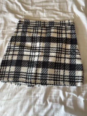 Rutig kortkjol  - Säljer en snygg rutig kortkjol från Primark i svart och vitt. Kjolen har en klassisk A-linjeform och är tillverkad i ett mjukt material som känns skönt mot huden. Perfekt att matcha med en stickad tröja eller boots för en trendig look.