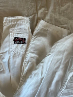 Vita jeans från Pepper Jeans - Säljer ett par vita jeans från Pepper Jeans med en snygg patch på bakfickan i brittisk stil. Klassisk femficksmodell och skön passform. Perfekta för dig som vill sticka ut med stilrena detaljer. Säljer ett till par i min profil. Står ingen storlek men passar mig som bär xs