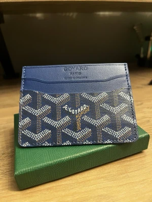 G plånbok - Säljer en elegant blå plånbok i klassisk design med ikoniskt mönster. Perfekt för dig som vill ha en stilren men samtidigt lite mer iögonfallande accessoar till vardags.  Plånboken är helt ny och oanvänd, i toppskick. Smidig storlek men med plats för kort och sedlar.