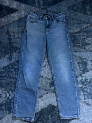 Blå raka jeans från Lee - Säljer ett par klassiska blå jeans från Lee med rak passform och fem fickor. Jeansen har en ljus tvätt och Lee-logga på bakfickan. Perfekta för en avslappnad stil och tillverkade i bomull.