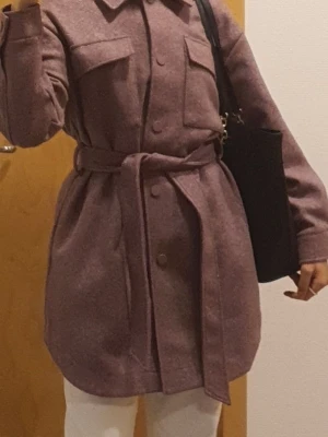 Ljuslila overshirt med bälte - Trendig ljuslila overshirt med bälte i midjan och stora bröstfickor. Jackan har knappar framtill, klassisk krage och lång ärm. Perfekt för lager-på-lager och en snygg vardagslook.
