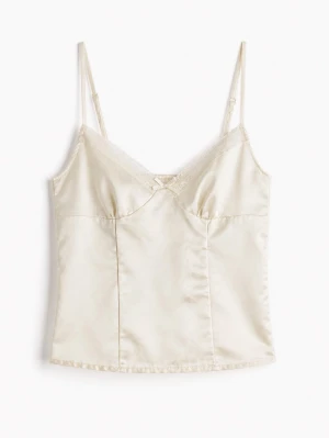 Krämfärgad satintopp med spets - Säljer en elegant krämfärgad topp i satin med tunna justerbara axelband och spetsdetaljer vid urringningen. Liten rosett framtill för en söt touch. Perfekt för dig som gillar en mjuk och lyxig känsla.