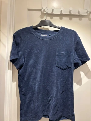 Mörkblå frotté t-shirt från Kappahl | S - En stilren mörkblå t-shirt från Kappahl i mjuk bomull. T-shirten har rund halsringning, korta ärmar och en bröstficka som ger en chill vibe. Perfekt för dig som gillar enkel och clean stil.