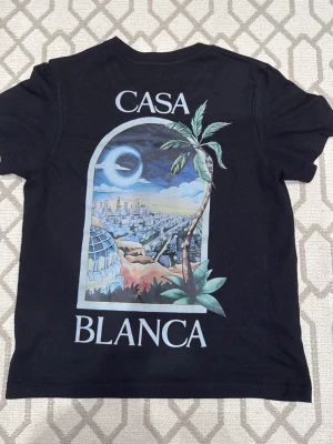 Svart Casablanca t-shirt med tryck - Svart t-shirt från Casablanca med färgglatt tryck av stadsmotiv och palm på både bröstet och ryggen. Klassisk rund hals och korta ärmar. Perfekt för dig som gillar streetwear med unik design.