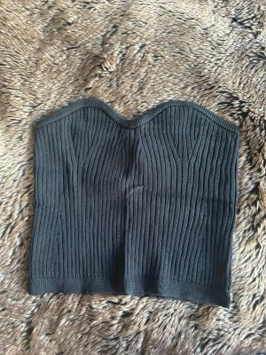 Svart ribbad tubtopp - Snygg svart ribbad tubtopp med hjärtformad överkant. Toppen är stickad och har en tight passform som framhäver figuren. Perfekt att styla med jeans eller kjol för en trendig look.