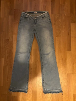 Ljusblå bootcut jeans med råa kanter - Säljer ett par ljusblå bootcut jeans med råa, fransiga kanter nertill. Jeansen har klassisk femficksdesign och normalhög midja. Perfekta för en avslappnad och trendig look. Materialet är denim i bomull. Lite slitna där nere men ingenting som syns jättemycket! Kom privat för frågor etc 💕