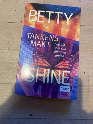 Tankens makt av Betty Shine - En inspirerande pocketbok av Betty Shine om tankens kraft och energi som kan förändra världen. Omslaget har färgstarka motiv med fjäril och hand i lila, orange och blå toner. Perfekt för dig som gillar personlig utveckling och andlighet.