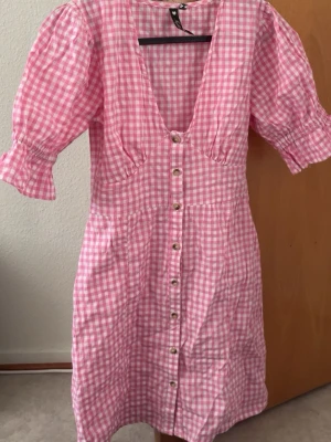 Rutig rosa klänning från Influence - Supersöt rosa och vit rutig klänning från Influence med knappar framtill och puffiga korta ärmar.