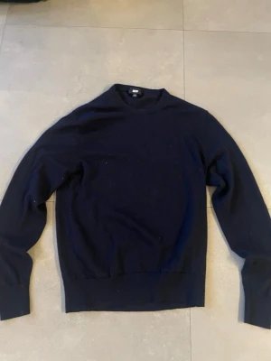 Mörkblå stickad tröja från uniqlo - En enkel och stilren mörkblå stickad tröja från uniqlo. Tröjan har rund halsringning, långa ärmar och ribbade muddar vid ärmslut och nederkant. Perfekt för lager-på-lager och passar till det mesta. Merinoull