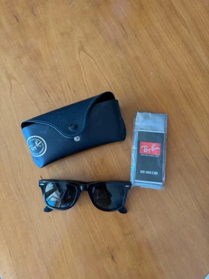 Svarta Ray-Ban Wayfarer solglasögon - Klassiska svarta Ray-Ban Wayfarer solglasögon med ikonisk fyrkantig form. Kommer med originalfodral och putsduk. Snygg och tidlös modell som passar till alla outfits. Bågarna är i svart plast och glasen är mörka.