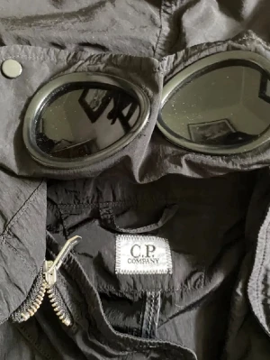 C.P. Company windbreaker med goggles - Svart vintage C.P. Company windbreaker från 2000 talet med ikoniska goggles i huvan. Jackan har flera fickor och knappar. Säljer pga har tröttnat på den och den är i gott skick👍Kom privat för frågor, prisförslag mm.