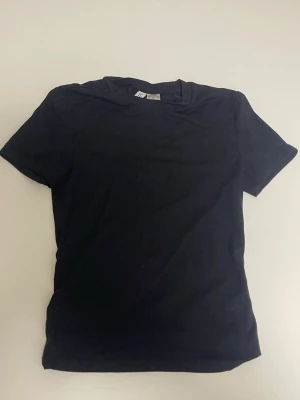 Svart basic t-shirt i bomull - Enkel svart t-shirt i mjuk bomull med klassisk passform och rund hals. Perfekt att matcha med jeans eller shorts för en clean och stilren look. Kortärmad modell utan tryck eller mönster.