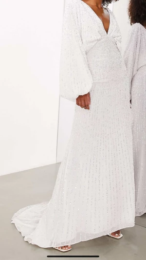 ASOS balklänning - slutsåld och viral - Elegant vit balklänning/ brudklänning med glittriga detaljer och djup v-ringning. Klänningen som trendat på Tiktok. Helt slutaåld online. Långa, puffiga ärmar och en vacker släp baktill. Perfekt för båda bal och bröllop. Endast använt i 2 timmar. 