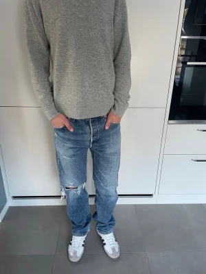 Levi's blå raka jeans med slitningar - Säljer ett par blå Levi's jeans med raka ben och coola slitningar på ena knät. Jeansen har fem fickor, normal midja och är tillverkade i bomull. Perfekta för en avslappnad och trendig look. Fakta!!                                                                 Modell: 501 vintage 1999.                             Längd:104-105 cm.                                     midja:41cm                                              benöppning: 20cm