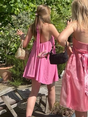 Rosa omlottklänning med knytband - Söt rosa kortklänning med omlott och knytband i nacken. Klänningen är ärmlös och har en luftig, A-linjeformad passform. Perfekt för varma dagar och somriga tillfällen.