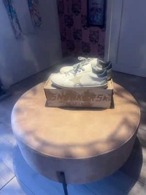 Golden goose - Snygga vita sneakers från Golden Goose med grå stjärna på sidan och gråa skosnören. Skorna har en låg profil och detaljer i silver vid hälen. Tillverkade i läder och har en klassisk streetstil som passar till det mesta.
