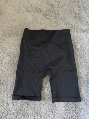 Svarta cykelshorts från NLY Sport - Svarta cykelshorts från NLY Sport med hög midja och tight passform. Tillverkade i ett stretchigt material som passar perfekt för träning. Diskret logga på ena benet. Snygga och bekväma shorts för en aktiv livsstil.