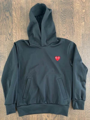 Comme Des Garçons Play Hoodie Men’s Small Black With Red Heart - Svart hoodie med huva och magficka från Comme des Garçons Play. Klassisk design med det ikoniska röda hjärtat med ögon broderat på bröstet. Nypris : ca 2000 SEK Pris : 400