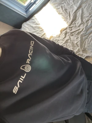 Marin blå Sail Racing sweatshirt - Marin blå sweatshirt från Sail Racing med vit logga tryckt på bröstet. Tröjan har rund halsringning, långa ärmar och ribbade muddar vid ärmslut och nederkant. Perfekt för en avslappnad och sportig stil.