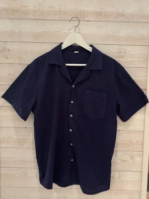 Mörkblå kortärmad skjorta - Stilren mörkblå skjorta med kort ärm och klassisk krage. Skjortan har knappar framtill och en bröstficka. Perfekt för en avslappnad look.