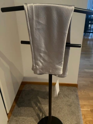 Silverfärgad midikjol i satin - Säljer en elegant silverfärgad midikjol från Vila i skimrande satinmaterial. Kjolen har en rak och slät form med diskret glans och är perfekt för dig som gillar stilrena plagg med lite extra lyxig känsla. Kjolen har inga synliga detaljer och är enkel att matcha.