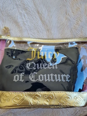 Juicy Couture transparent väska - Snygg transparent väska från Juicy Couture med guldfärgade detaljer och texten 'Juicy Queen of Couture' i guld och strass. Väskan har guldfärgad dragkedja och dekorativt kronhänge. Perfekt för att hålla koll på dina essentials.