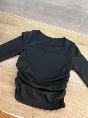 Svart ribbad långärmad topp - Svart långärmad topp med rund halsringning och ribbad struktur. Toppens material är stretchigt och följsamt, perfekt för en stilren och enkel look. Passar till många olika outfits och är ett måste i garderoben.