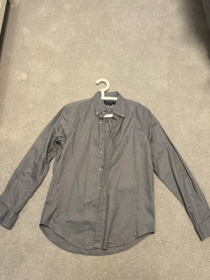 Blå skjorta från Ralph Lauren - Klassisk blå skjorta från Ralph Lauren med broderad logga på bröstet. Skjortan har lång ärm, knappar framtill och en tidlös passform. Perfekt för dig som gillar stilrena och ikoniska plagg.