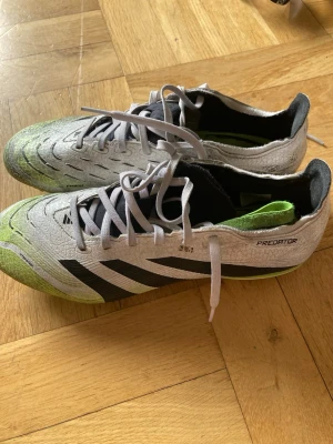 Adidas Predator fotbollsskor vit/svart str. 41 1/3 - Säljer ett par Adidas Predator fotbollsskor i vitt med svarta detaljer och limegröna inslag. Skorna har snörning, låg profil och dobbar för spel på gräs. Tillverkade i syntetmaterial för bra grepp och kontroll på planen. Perfekta för dig som vill dominera mittfältet. Storlek 41 1/3 (25,5 cm)