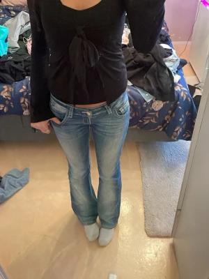 Svart långärmad topp med knyt - Snygg svart långärmad topp med knyt framtill och djupare ringning. Modellen är figurnära och toppen har en croppad känsla. Perfekt att matcha med jeans eller kjol för en trendig look.