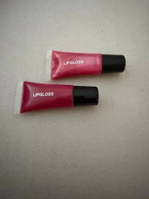 Rosa läppglans i tub 6,5 ml - Två rosa läppglans i smidig tub med svart skruvkork. Ger glansiga och fylliga läppar med en hint av rosa färg. Varje tub innehåller 6,5 ml och är enkel att ta med i väskan. Perfekt för dig som vill ha glansiga läppar med färg. Finns mindre kvar, har används.