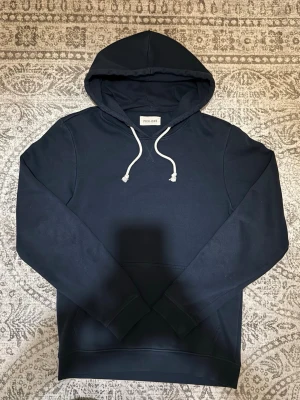 Mörkblå hoodie från Pier One - Snygg mörkblå hoodie från Pier One med klassisk design. Hoodien har vita dragsnören och en stor känguruficka framtill. Tillverkad i mjukt bomullsmaterial som är skönt att ha på sig. Perfekt för en avslappnad och stilren look.