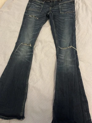 Mörkblå bootcut jeans med slitningar - Snygga mörkblå bootcut jeans med slitningar över knäna och lätt tvättad look. Jeansen har klassiska fem fickor och utsvängda ben. Perfekta för en avslappnad och trendig stil. Gina tricot 