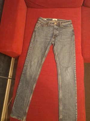 Blå raka jeans från Jack & Jones - Säljer ett par klassiska blå jeans från Jack & Jones med rak passform och fem fickor. Jeansen har normal midja, gylf med dragkedja och knapp samt kontrastsömmar. Perfekta till en avslappnad stil och tillverkade i slitstark denim.