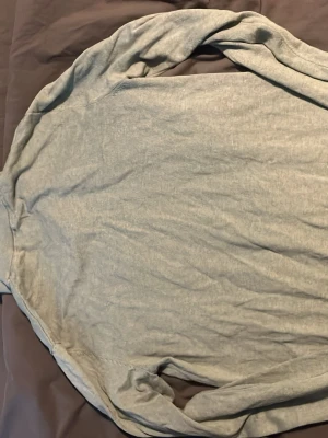 Grön tröja med halv dragkedja - Snygg ljusgrå långärmad tröja från J.Lindeberg med halv dragkedja och ståkrage. Tröjan har ribbade muddar vid ärmslut och nederkant, perfekt för en stilren och avslappnad look. Materialet känns mjukt och lätt.